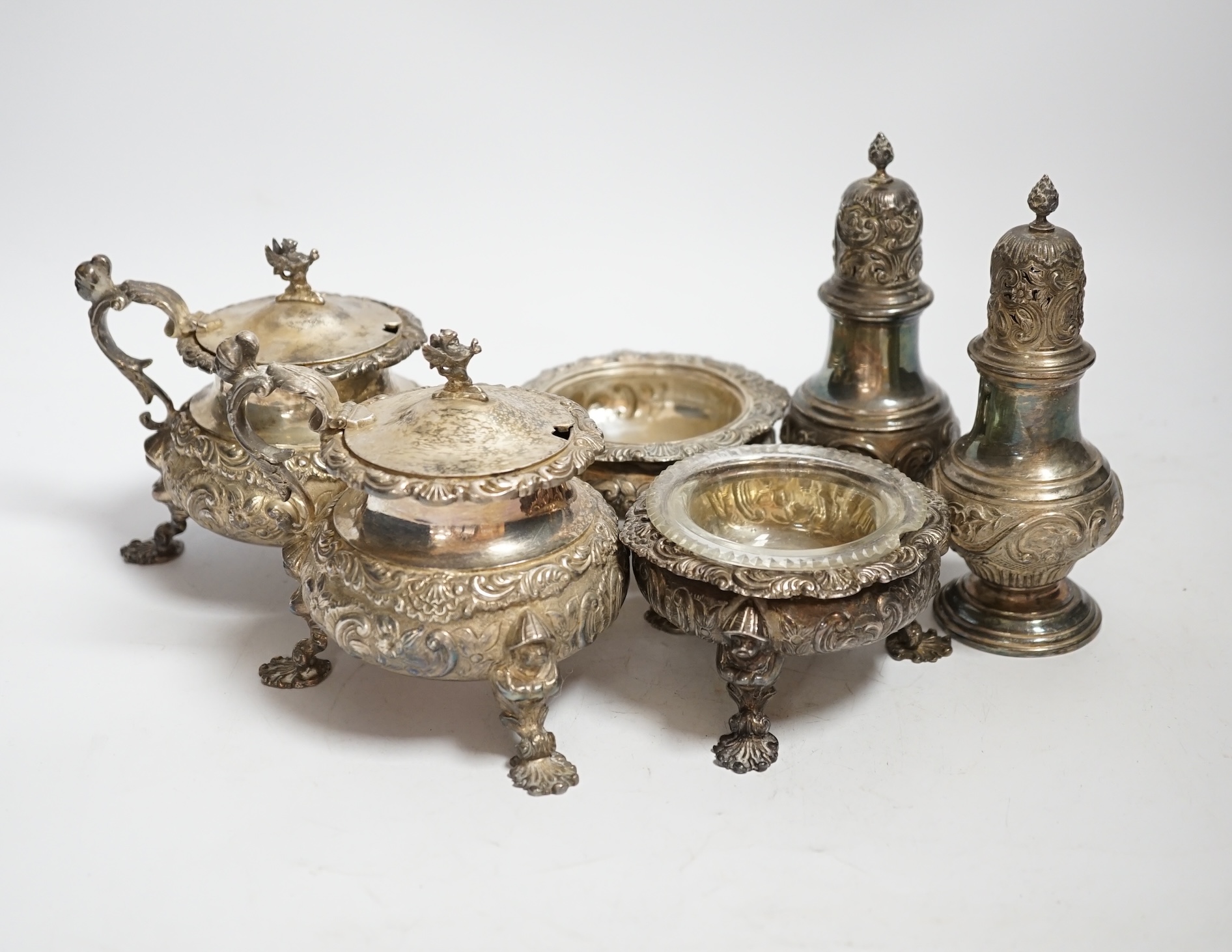 An ornate Edwardian silver four piece condiment set, with chinoiserie decoration by William Comyns, comprising two mustard pots and two salts, one with glass liner and a pair of similar pepperettes, all London, 1906, sal